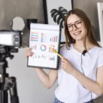 young-blogger-recording-with-professional-camera-holding-clipboard-with-graphics-1